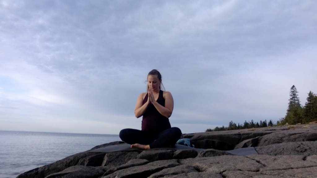 A silhouette of someone practicing yoga at sunrise by the serene shores of Lake Superior.