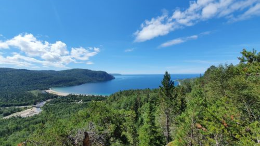 A scenic view of a well-trodden hiking trail winding through the dense forests around Lake Superior, with the lake glistening in the distance.